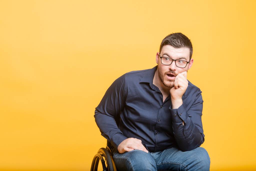 Oliver has short, dark hair. Wearing glasses and a navy blue button up shirt. Leaning on his elbow with his chin on his hand. A perplexed facial expression