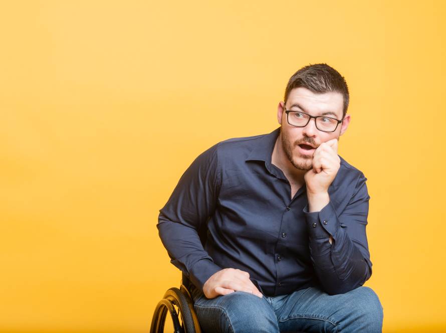 Oliver has short, dark hair. Wearing glasses and a navy blue button up shirt. Leaning on his elbow with his chin on his hand. A perplexed facial expression